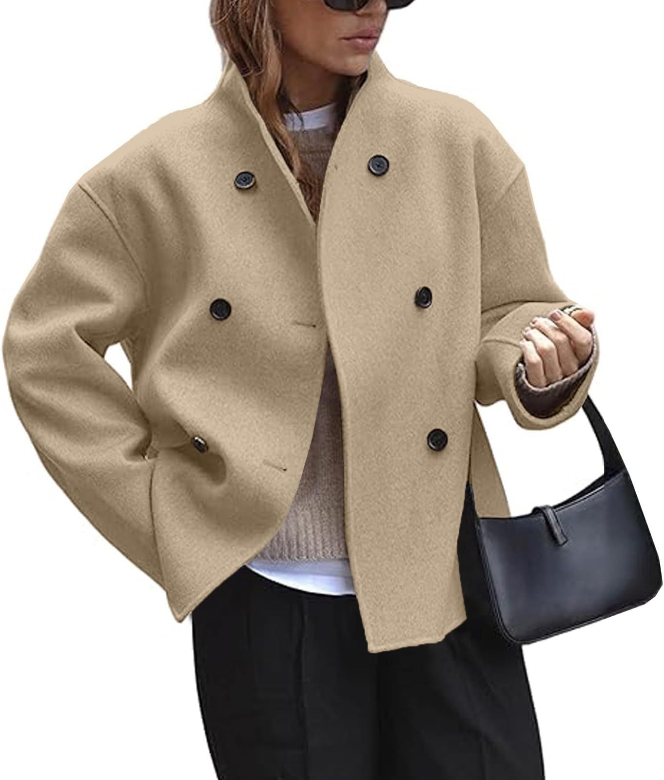 Person wearing a beige peacoat with black buttons, holding a black handbag on a white background